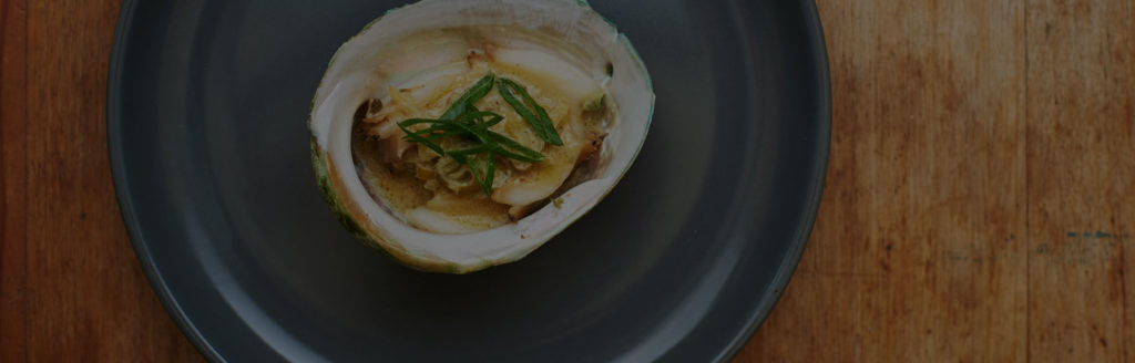 A single Poached Abalone with White Wine and Cream is served on a black dish.