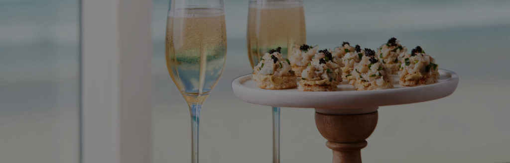 Minced abalone canapés sit atop a serving platter, with two glasses of sparkling white wine in the background.