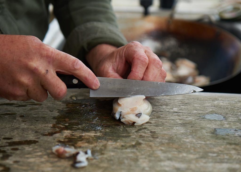 A man trims defrosted abalone using a sharp Japanese knife.