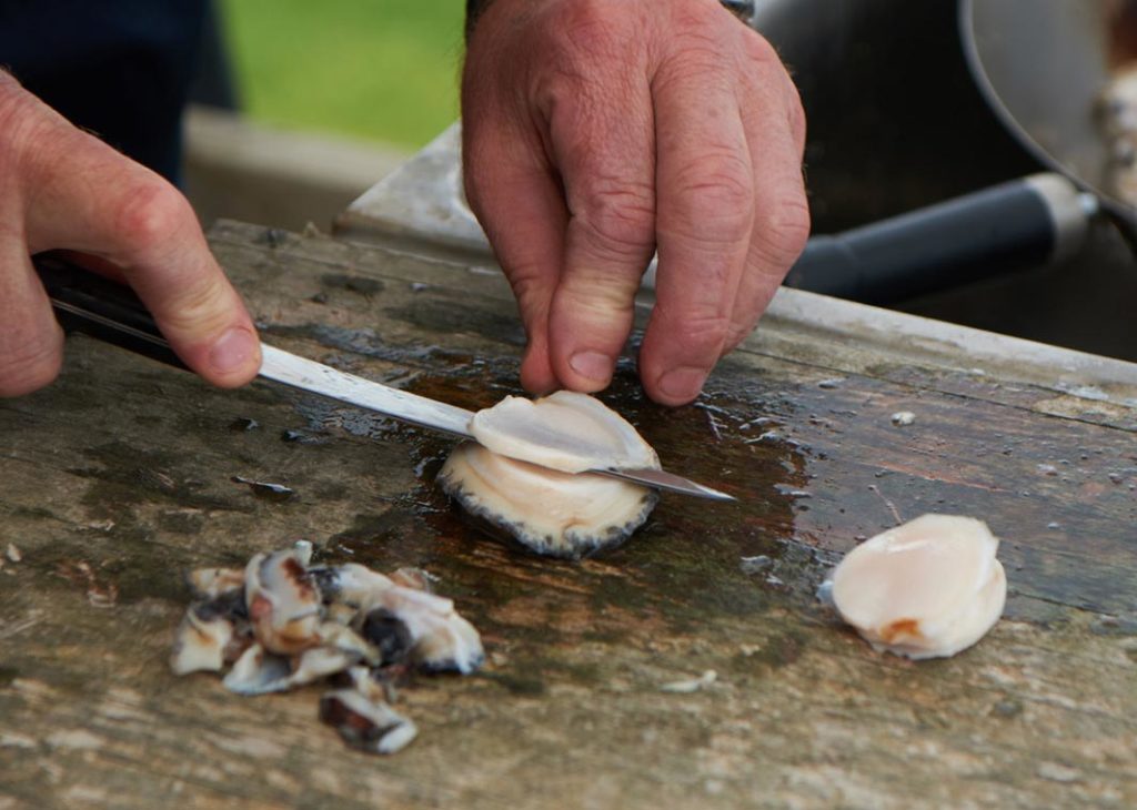 A man thinly slices cleaned Australian abalone on a wooden work surface.