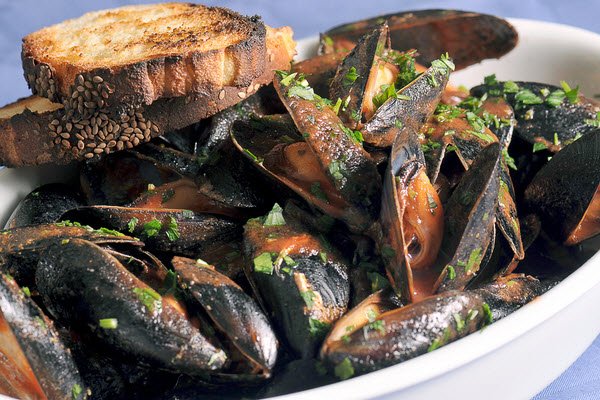 Kinkawooka Chilli Mussels served in a white bowl with charred bread to the side.
