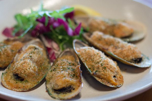Kinkawooka Mussels with Miso Butter, served on a white plate with salad behind.
