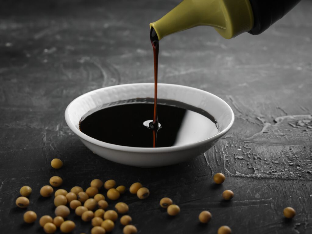 Pouring soy, honey and ginger dressing into a white ceramic bowl.